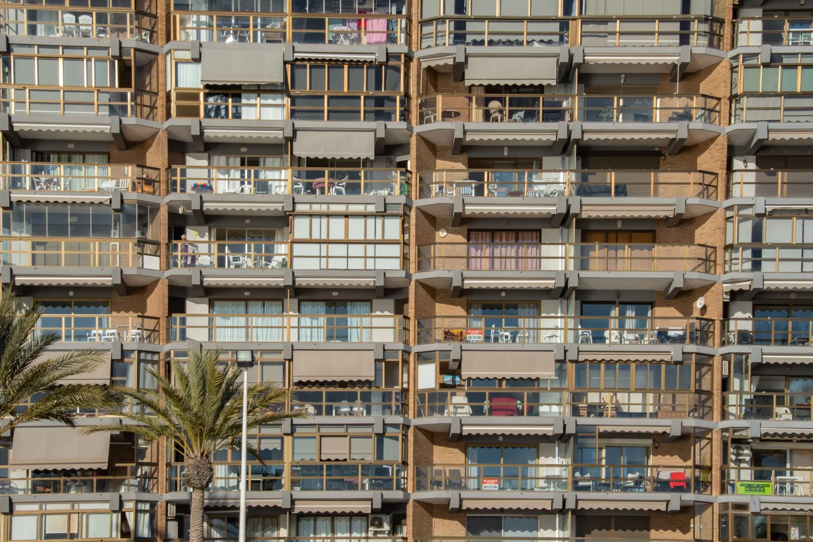 Fachada de un bloque de apartamentos en España con terrazas y carteles de venta en varias viviendas