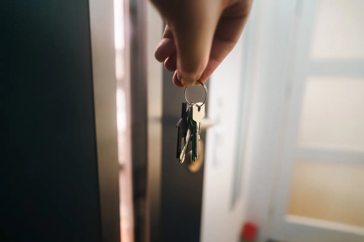 Mano entregando las llaves de una vivienda en la puerta de un piso de alquiler
